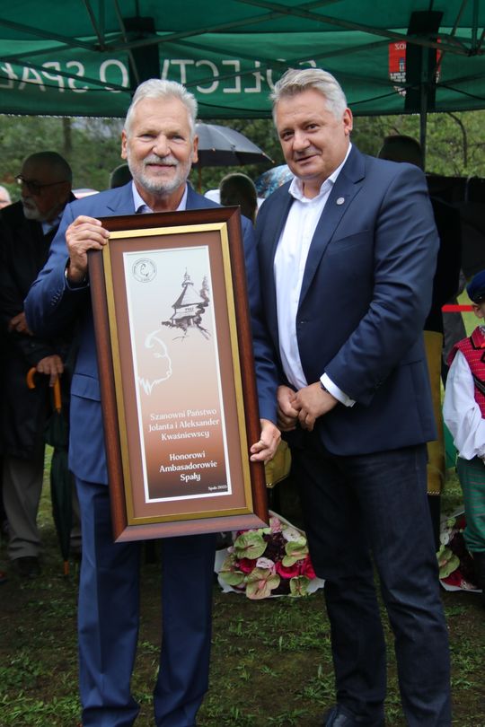 Uhonorowanie tytułem „Honorowi Ambasadorowie Spały” Dwóch mężczyzn trzyma dużą, oprawioną tablicę z napisem „Honorowi Ambasadorowie Spały” podczas ceremonii.