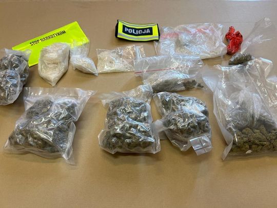 Zabezpieczone przez policję worki z suszem roślinnym i porcjami białego proszku na stole.