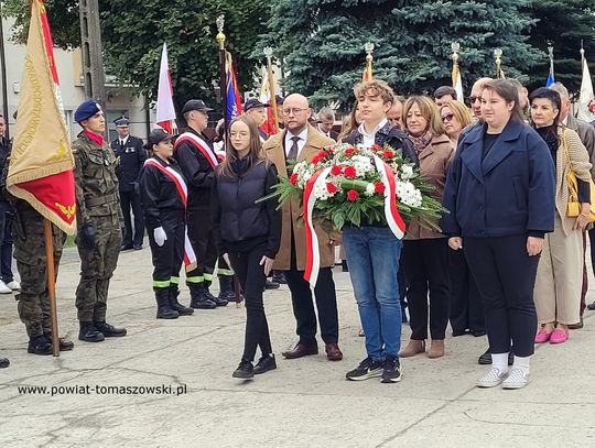 Młodzież i mieszkańcy niosą wieniec, a obok stoją poczty sztandarowe podczas obchodów 86. rocznicy Polskiego Państwa Podziemnego.