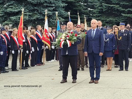 Złożenie wieńca przez przedstawicieli powiatu; w tle poczty sztandarowe i funkcjonariusze służb.