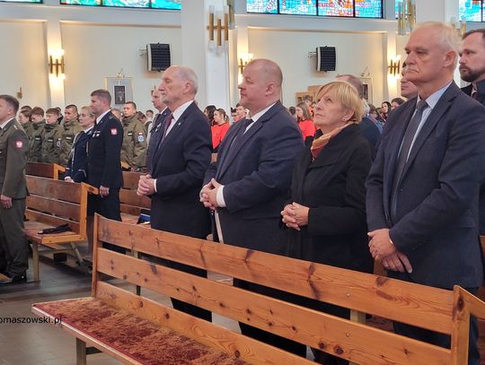 Przedstawiciele władz samorządowych i służb mundurowych stoją w ławkach podczas mszy rocznicowej.