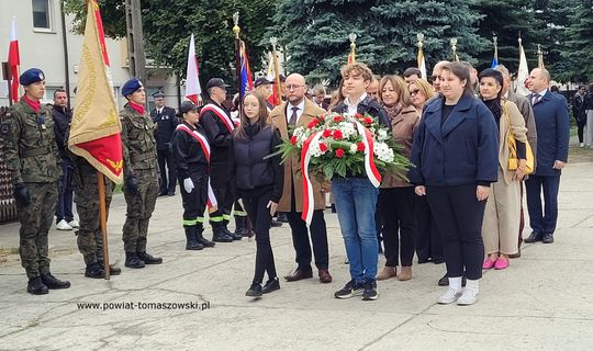 Młodzież i mieszkańcy niosą wieniec, a obok stoją poczty sztandarowe podczas obchodów 86. rocznicy Polskiego Państwa Podziemnego.