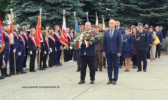 Złożenie wieńca przez przedstawicieli powiatu; w tle poczty sztandarowe i funkcjonariusze służb.