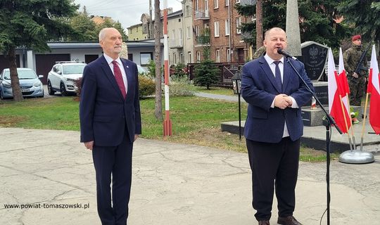 Wystąpienia przy pomniku; uczestnicy uroczystości słuchają przemówień w plenerze.